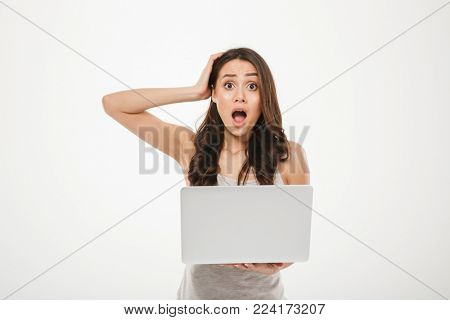 Photo of uptight woman 30s looking on camera and grabbing her head with open mouth while using silver notebook isolated over white wall
