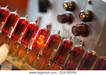 hand holds a block of red vintage nixie tubes (electronic components) on the background of a measuring device, power supply.