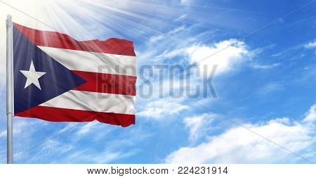 Flag of Puerto Rico on flagpole against the blue sky.