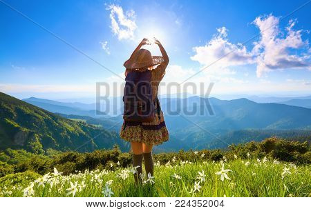 The lawn with white daffodils in the high mountains landscapes. The girl in overknees stockings, romantic dress, back sack and straw hat. A place to relax in the Carpathian Park.