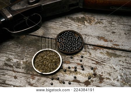 Shotgun rifle with gunpowder and many plumbeous fractions lead shot on wooden table background, top view. Hunting equipment close-up.