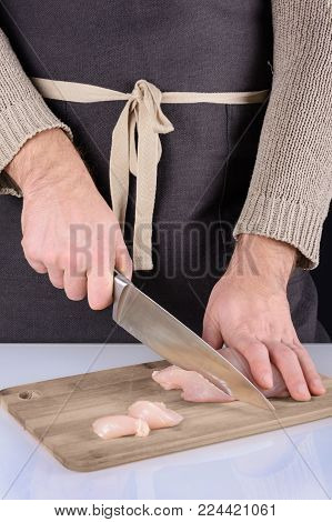 A man in an apron is cutting meat on a wooden board. Chicken making. Preparation of healthy food.