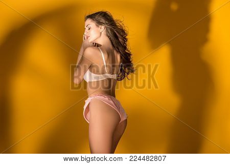 side view of sexy girl standing in lingerie set with shadow silhouette on wall on orange