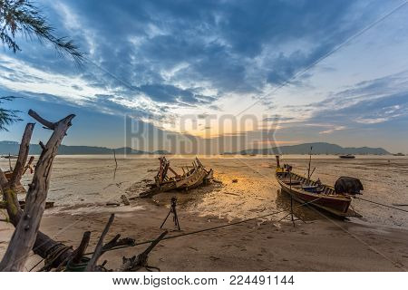 Fishing boat at the beach (long-tail boats) and boat carcass in low water and the beautiful sunrise at Phuket Island, Thailand.