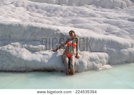 Beautiful Girl In Orange Swimsuit Stands Near White Stone At Pamukkale. Province Of Denizli In The S