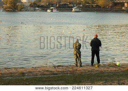 Fisherman and friend in autumn day fishing on river