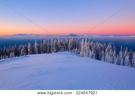 Landscape with high mountains covered with snow. Interesting frozen texture. Beautiful winter sunrise with orange blue sky. Place for tourists. Christmas story.