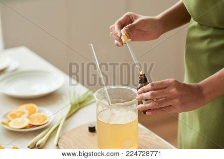 Hands of woman adding essential oil into melted soap base