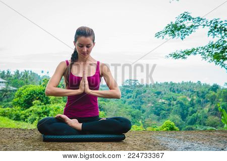 Lotus pose on green nature background. Woman meditates in yoga asana Padmasana