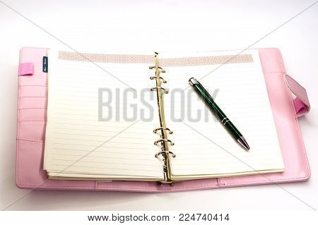 pink notebook with a ballpoint pen lying on white background
