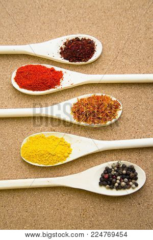 Cooking hot spicy meal. A set of four different spices in wooden spoons, corkwood background, top view