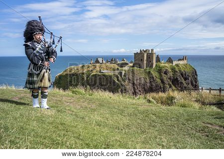 Traditional scottish bagpiper in full dress code at Dunnottar Castle in Stonehaven