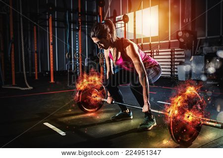 Determined athletic girl works out at the gym with a fiery barbell