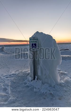 Thick ice taller than the parking sign is protecting the handicap parking space at the edge of Lake Michigan