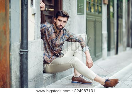 Young Bearded Man, Model Of Fashion, Sitting In An Urban Step Wearing Casual Clothes.