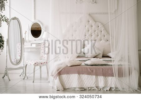 White Bedroom Interior With Nobody. Large Cozy Bed With A White Canopy And Oval Dressing Mirror With