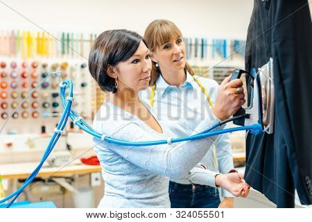 Two women in a dry-cleaning company ironing clothes on a hanger