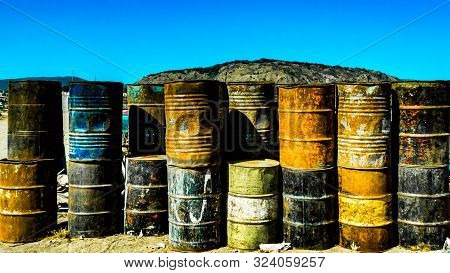 Multi-colored, Rusty And Old Oil Barrels In Piles With A Blue Sky And Sunny Day In Mexico