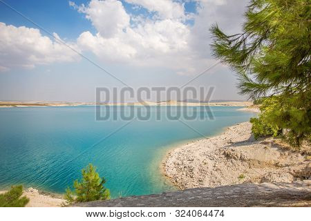 White Coast With Turquoise Water And Green Pine Trees And Clouds. Reservoir On The Euphrates River