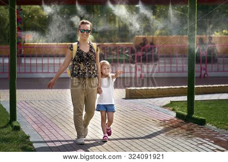 Young Mother With Her Daughter In Hot Weather, Cool Off At The Gates Of Climate Control In The Water