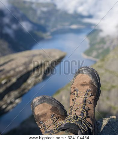 Hiking Boots In Foreground. Troll Tongue (trolltunga) And Norway Fjord In The Background.