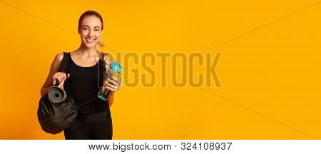 Woman Holding Fitness Bag, Rolling Mat And Water Ready For Training. Yellow Background, Studio Shot,