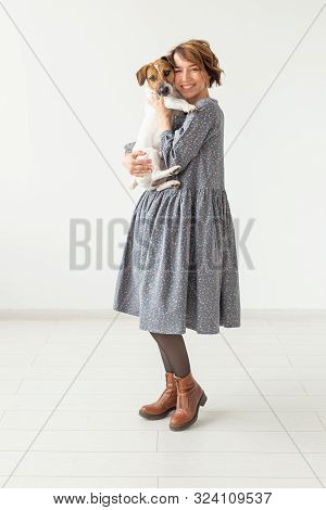Charming Smiling Young Woman In A Stylish Gray Dress Holding Her Favorite Dog Jack Russell Terrier. 