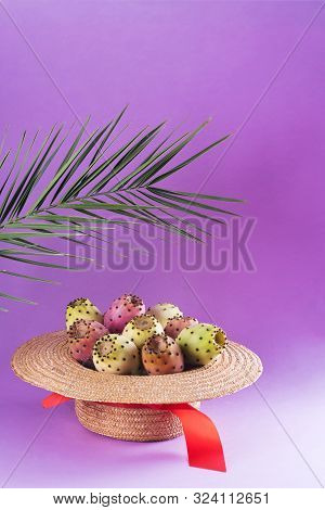 Opuntia Fruit In A Straw Hat With A Palm Leaf On A Trendy Purple Background. Prickly Pear Or Fichi D
