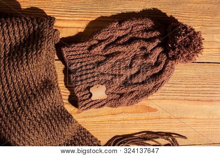 Brown Knitted Hat And Scarf On A Wooden Background With Natural Light Shadow. Trendy Winter Accessor