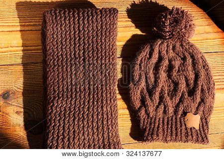 Brown Knitted Hat And Scarf On A Wooden Background With Natural Light Shadow. Trendy Winter Accessor