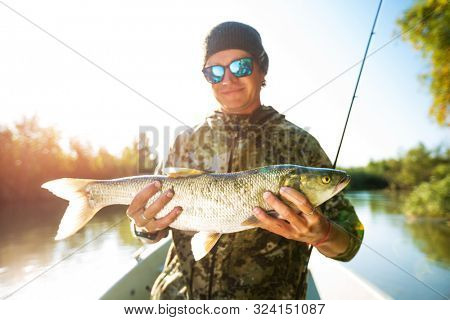 Happy angler holds Asp fish (Aspius aspius) being on the boat and smiles. Astrakhan region, Russia
