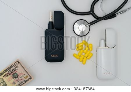 Iqos, Stethoscope, Yellow Tablets And Dollar On A White Background. The Concept Of Health Damage Fro