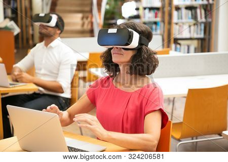Group Of Adult Students Using Vr Simulator In Library. Middle Aged Woman In Virtual Reality Headset 