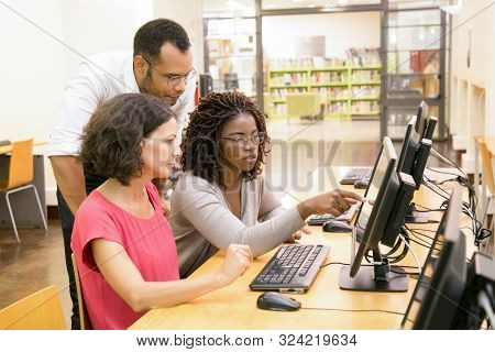 Trainer Helping Students In Computer Class. Man And Women Sitting And Standing At Desk, Using Deskto