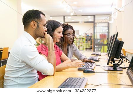 Diverse Team Of Adult Students Working Together In Computer Class. Man And Women In Casual Sitting A