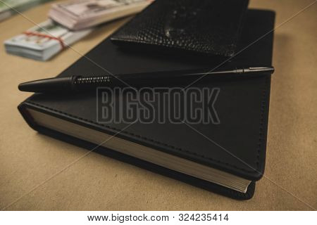 A Black Notebook , A Pen And Dollar Cash Banknotes On Wooden Background - Concept Of Financial Manag
