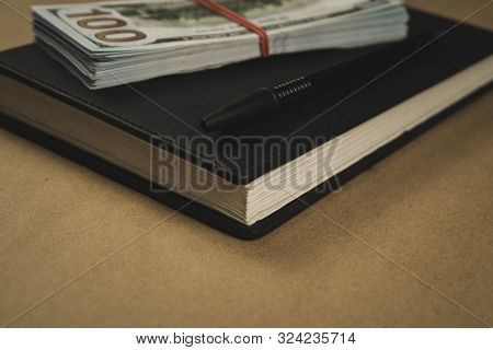 A Black Notebook , A Pen And Dollar Cash Banknotes On Wooden Background - Concept Of Financial Manag
