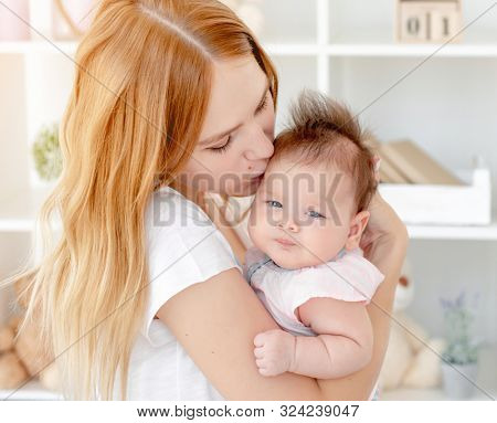 Happy mother kissing cute baby holding her up