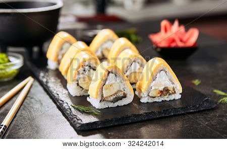 Macro shot of tropical sushi rolls with banana, eel, rice, cream cheese and processed cheese on black background. Eating fusion uramaki sushi with selective focus closeup in Japanese restaurant