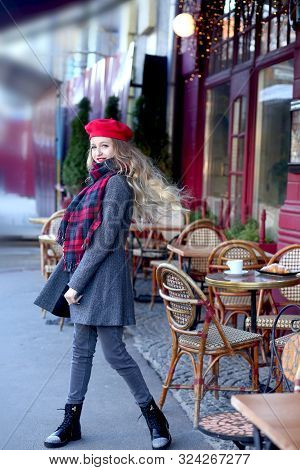 Girl With A Street In A Gray Coat With Long Curls Is Spinning Near A Cafe