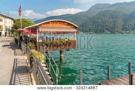 View Of Picturesque Village Morcote With Outdoor Bars And Gift Shops On The Shore Of Lake Lugano In