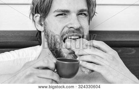 French Breakfast Stereotype. Handsome Man Browsing Internet In Bed. Guy Having Coffee And Holds Croi
