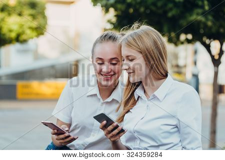 Happy   Moments Of Two Stylish Girls Hugging And Looking At The Phone, Discussing Something On The S