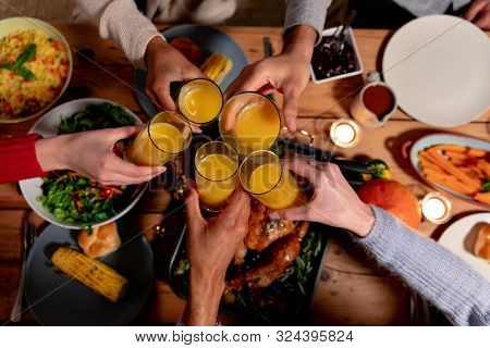 Overhead view of the hands of a group of young adult multi-ethnic male and female friends sitting at a table at home set for Thanksgiving dinner making a toast with glasses of orange juice