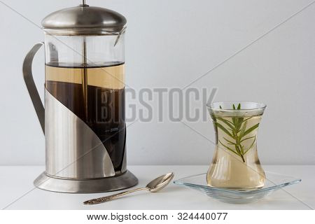 Rosemary Tea In Armudu Glass With Branch Of Rosemary In It, Teapot And Spoon On The Table On White B