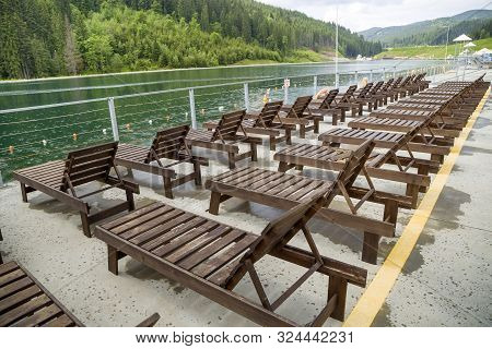 Row Of Empty Wooden Beach Chairs Near Water.
