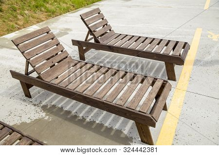 Row Of Empty Wooden Beach Chairs Near Water Outdoors.