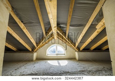 Attic Of A Building With Wooden Beams Of A Roof Structure And A Small Window.