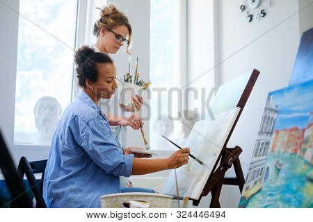 Creative painter and her protege working in a studio