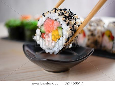 Close Up Of Sushi Maki Roll With Salmon, Snow Crab And Vegetables In Chopsticks With Soy Sauce. Vari